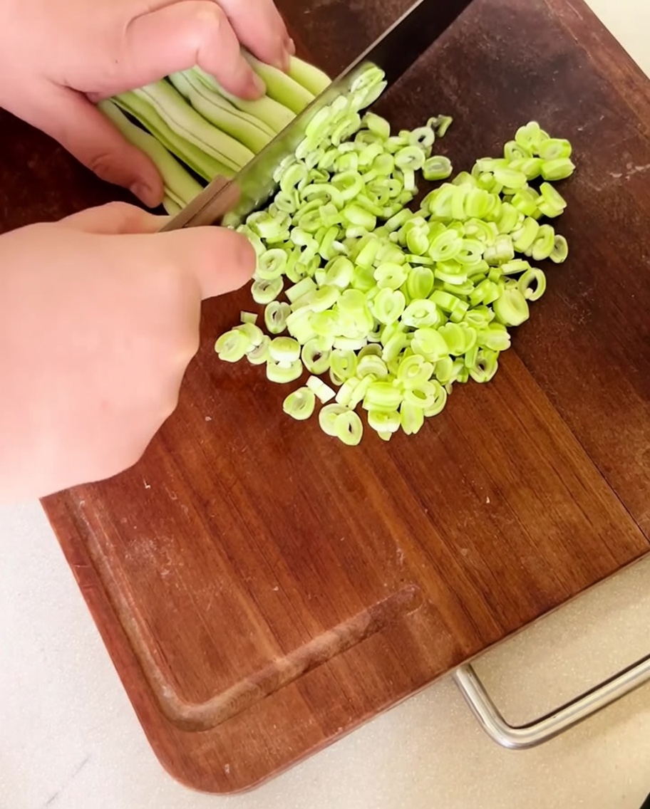 Fagioli freschi tritati finemente distribuiti su un tagliere di legno.