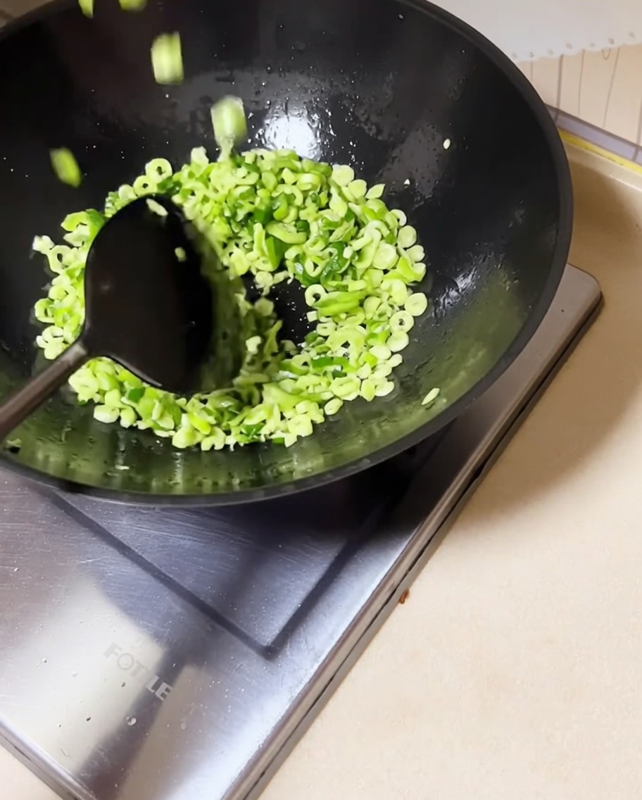Fagioli tritati mescolati nel wok con i cipollotti soffritti.