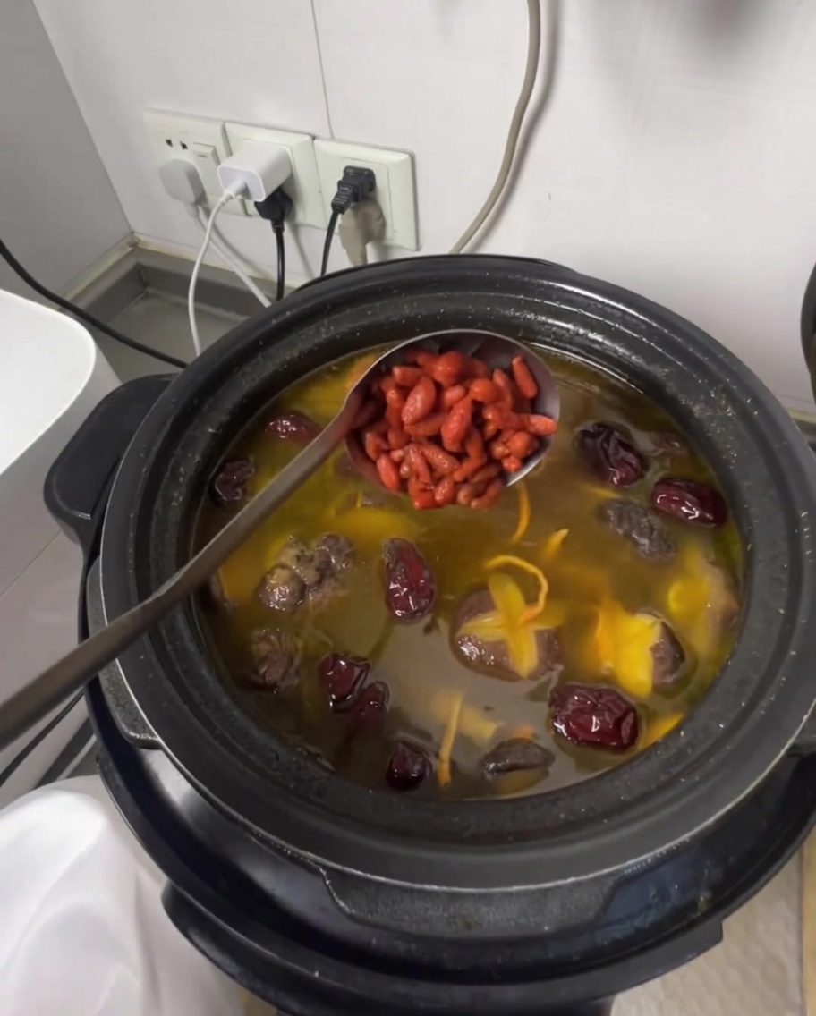 Un mestolo che aggiunge bacche di goji nella zuppa di pollo profumata.