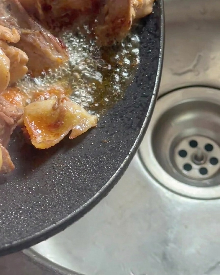 Wok inclinato che versa il grasso di pollo sciolto nel lavandino.