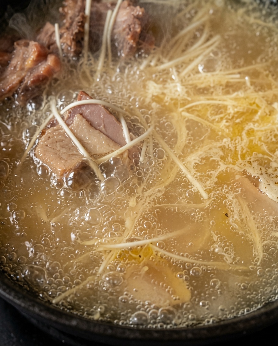 Noodles che cuociono in una pentola di ricca zuppa di pollo bianca e bollente.