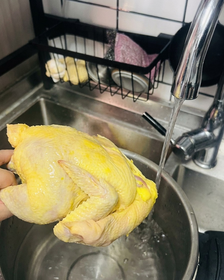 Una mano che tiene una gallina intera sotto lacqua corrente, pronta per essere messa in una pentola con acqua calda.