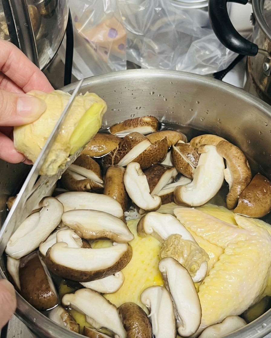 Una persona che affetta zenzero fresco direttamente sopra una pentola di pollo e funghi.