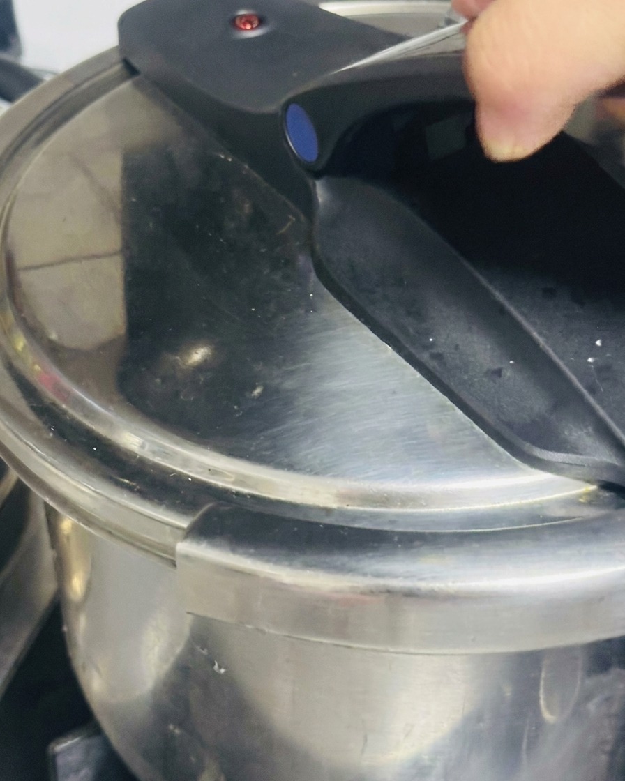 Una mano che chiude e blocca saldamente il manico di una pentola a pressione in acciaio inossidabile.
