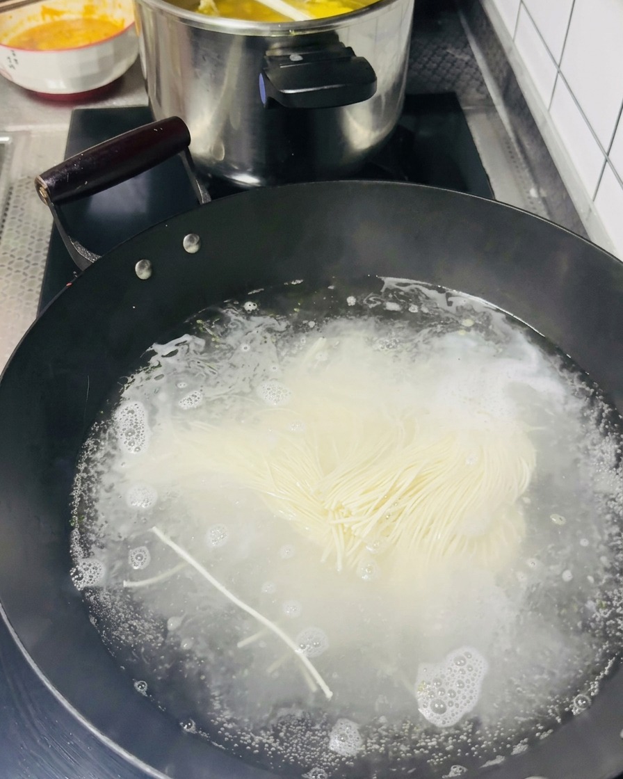Un mazzetto di noodles sottili che viene immerso in un wok con acqua bollente.