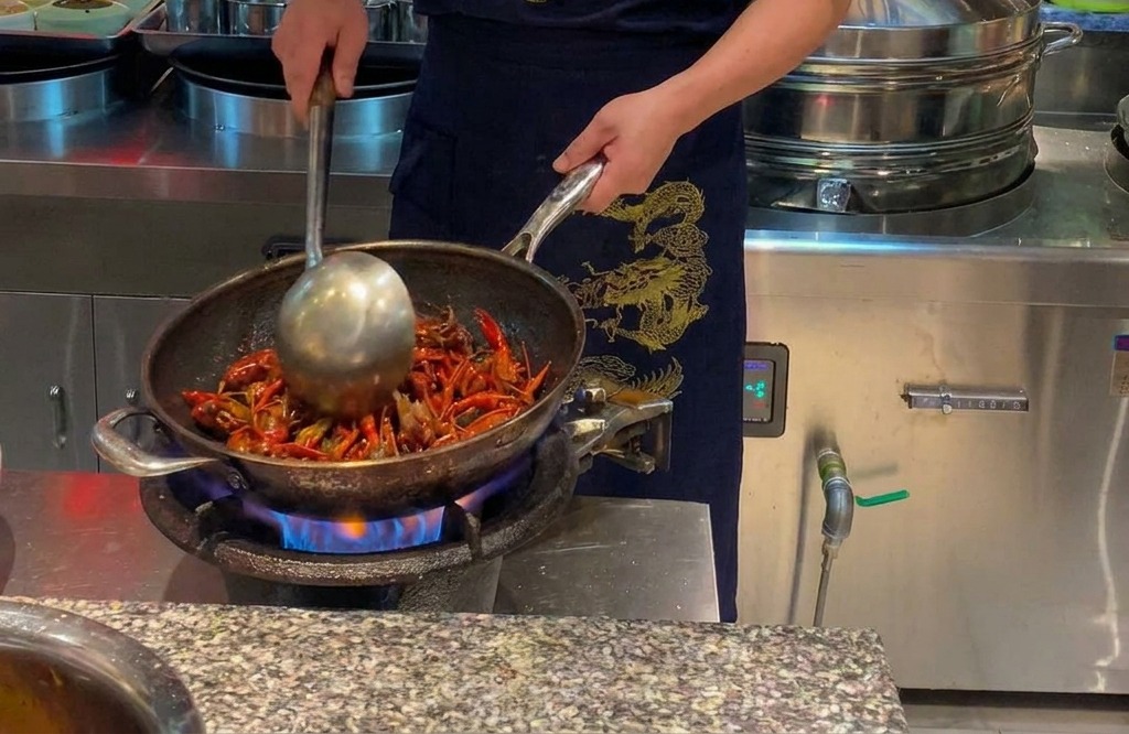 Uno chef che salta gamberi di fiume di un rosso acceso in un grande wok su fiamma viva.