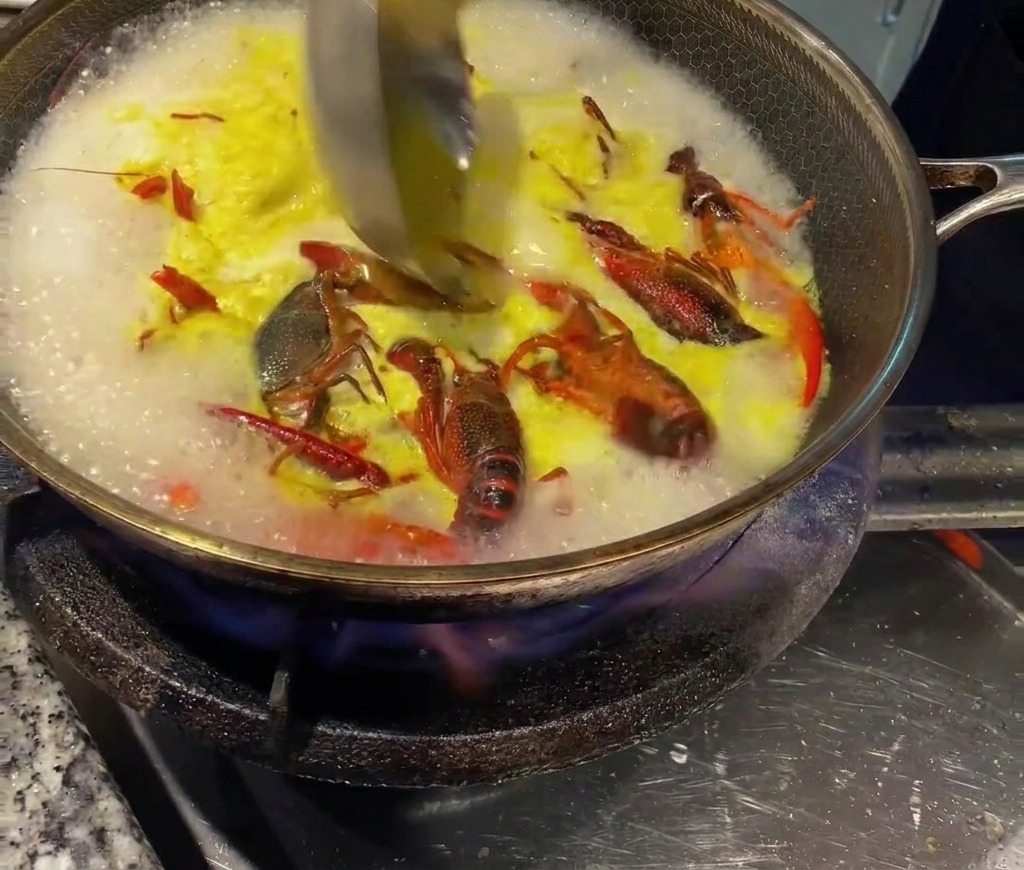 Un mestolo che mescola il brodo di pollo concentrato nel brodo caldo dei gamberi.