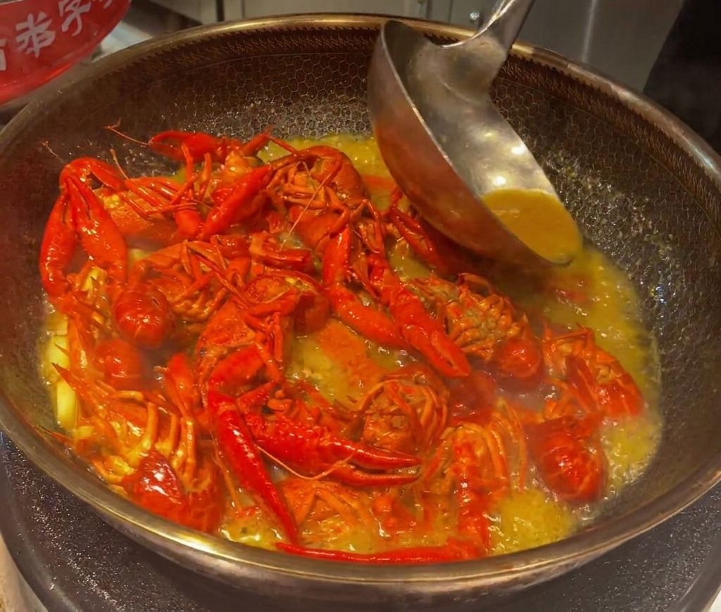 Gamberi di fiume che sobbollono e vengono mescolati in un denso brodo ridotto e saporito in un wok.