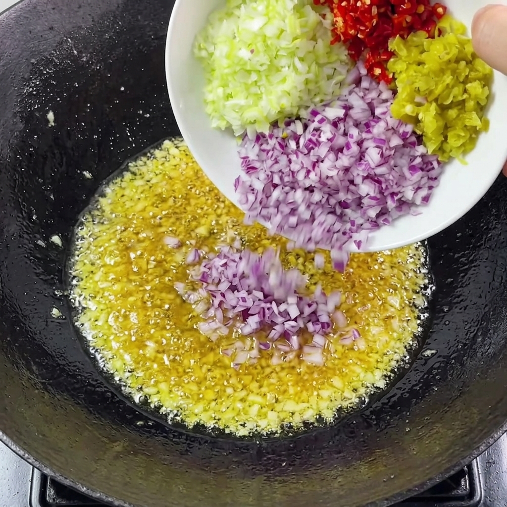 Cipolle tritate, cipollotti e peperoncini aggiunti allaglio nel wok.