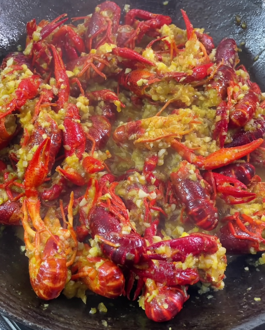Aglio tritato, curry in polvere e condimenti aggiunti a un wok di gamberi in cottura.