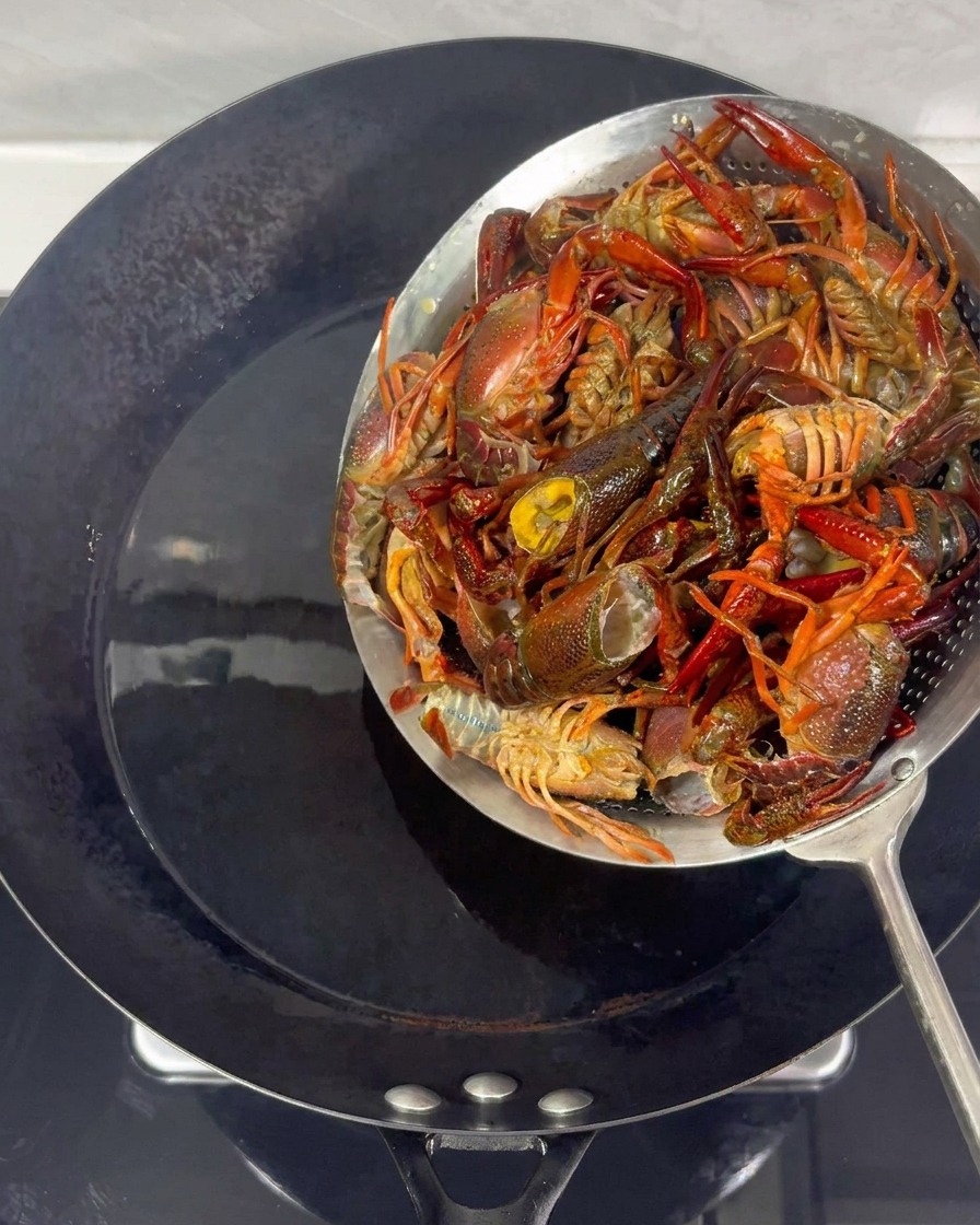 Gamberi rimossi dallolio bollente in un wok usando un colino di metallo.