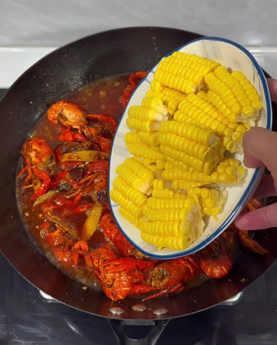 Pezzi di mais disposti nel brodo piccante in ebollizione con i gamberi in un wok.