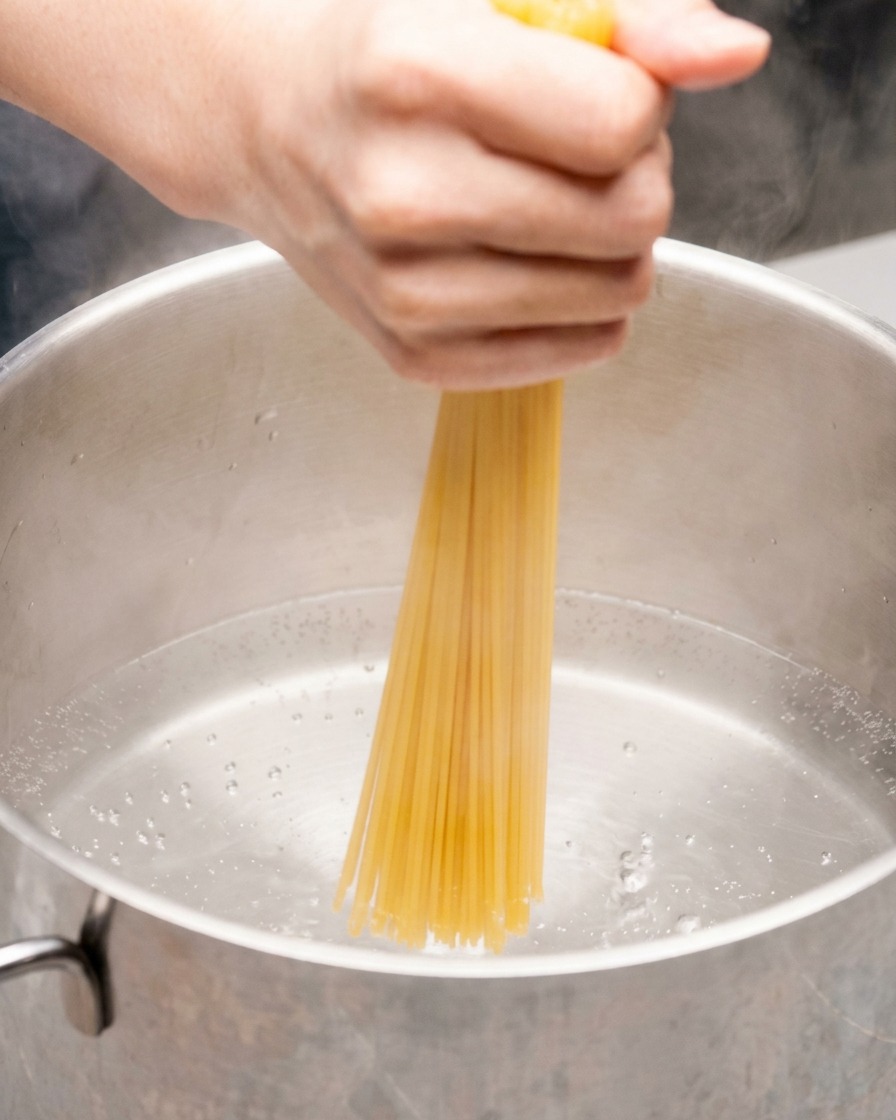 Una mano che immerge un mazzo di spaghetti secchi in una pentola di acqua bollente.