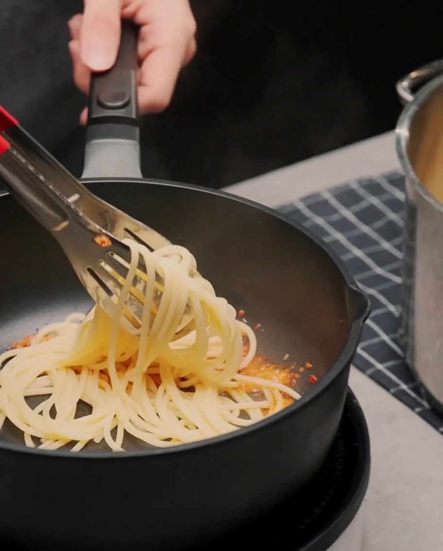 Spaghetti cotti saltati con le pinze in una padella con olio allaglio e peperoncino.