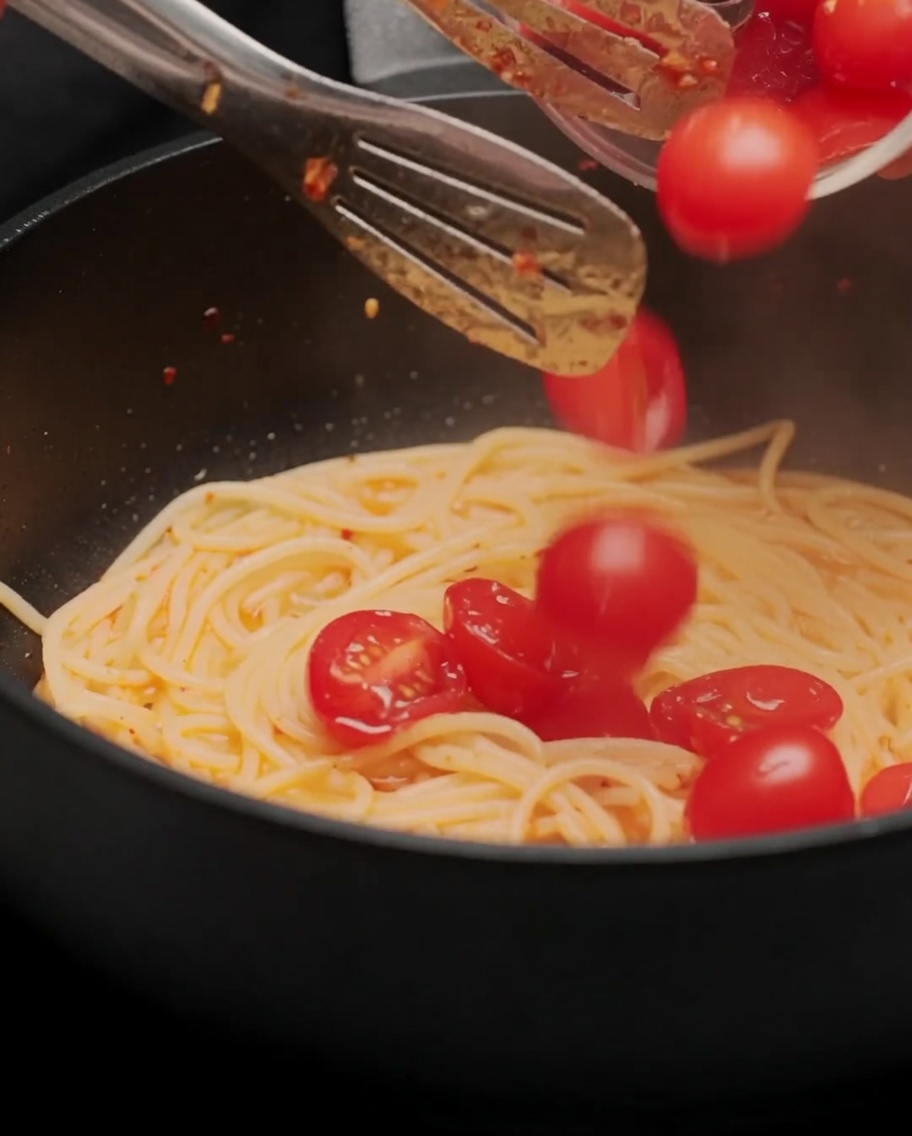 Pomodorini tagliati a metà aggiunti alla padella con gli spaghetti.