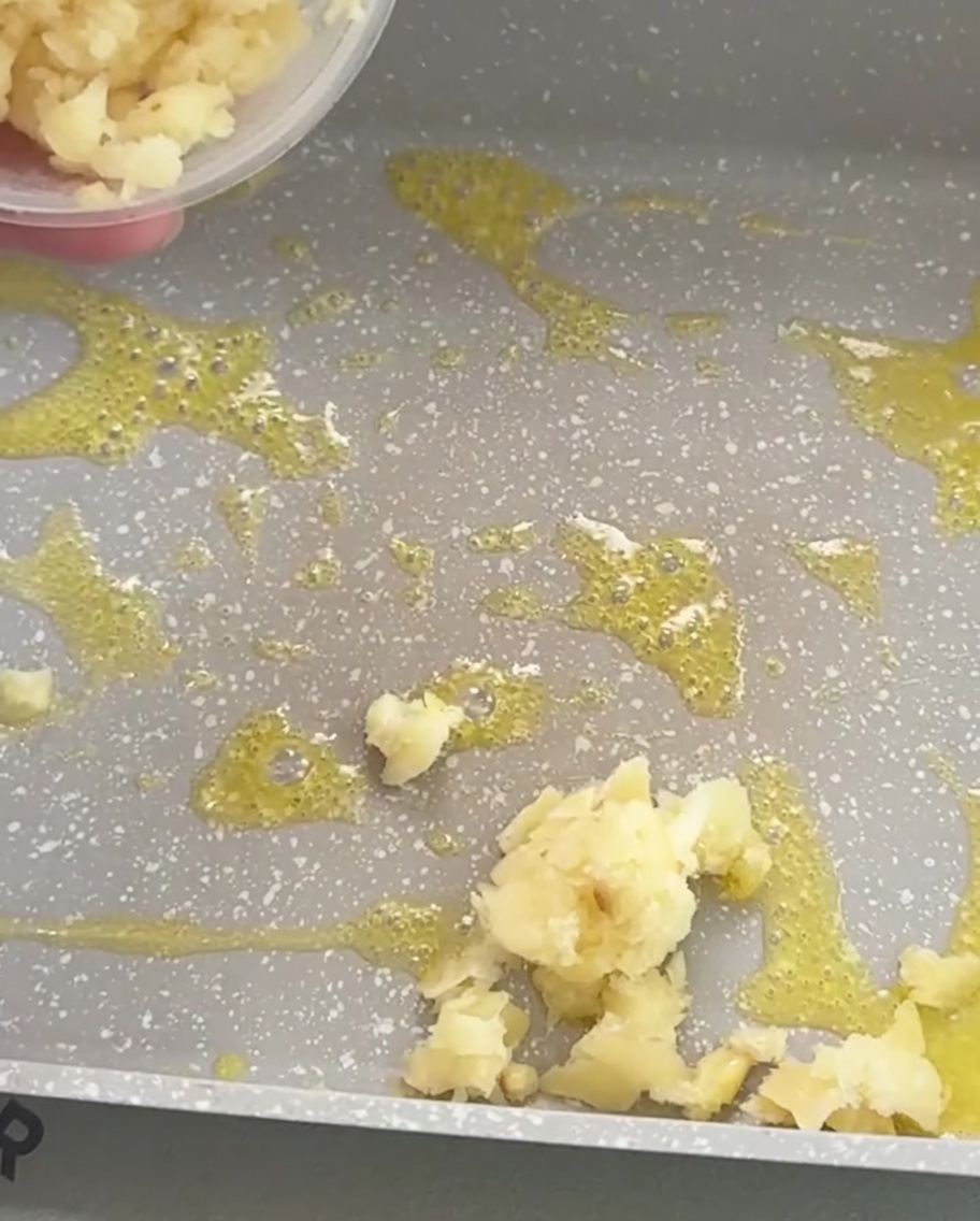 Aglio tritato che frigge nel burro fuso allinterno di una padella rettangolare, dorandosi leggermente.
