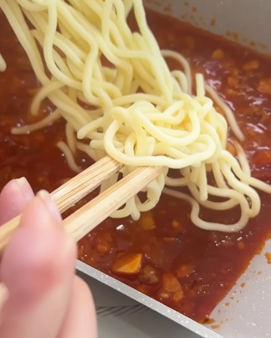 Spaghetti saltati in padella con il ragù di carne utilizzando delle bacchette.