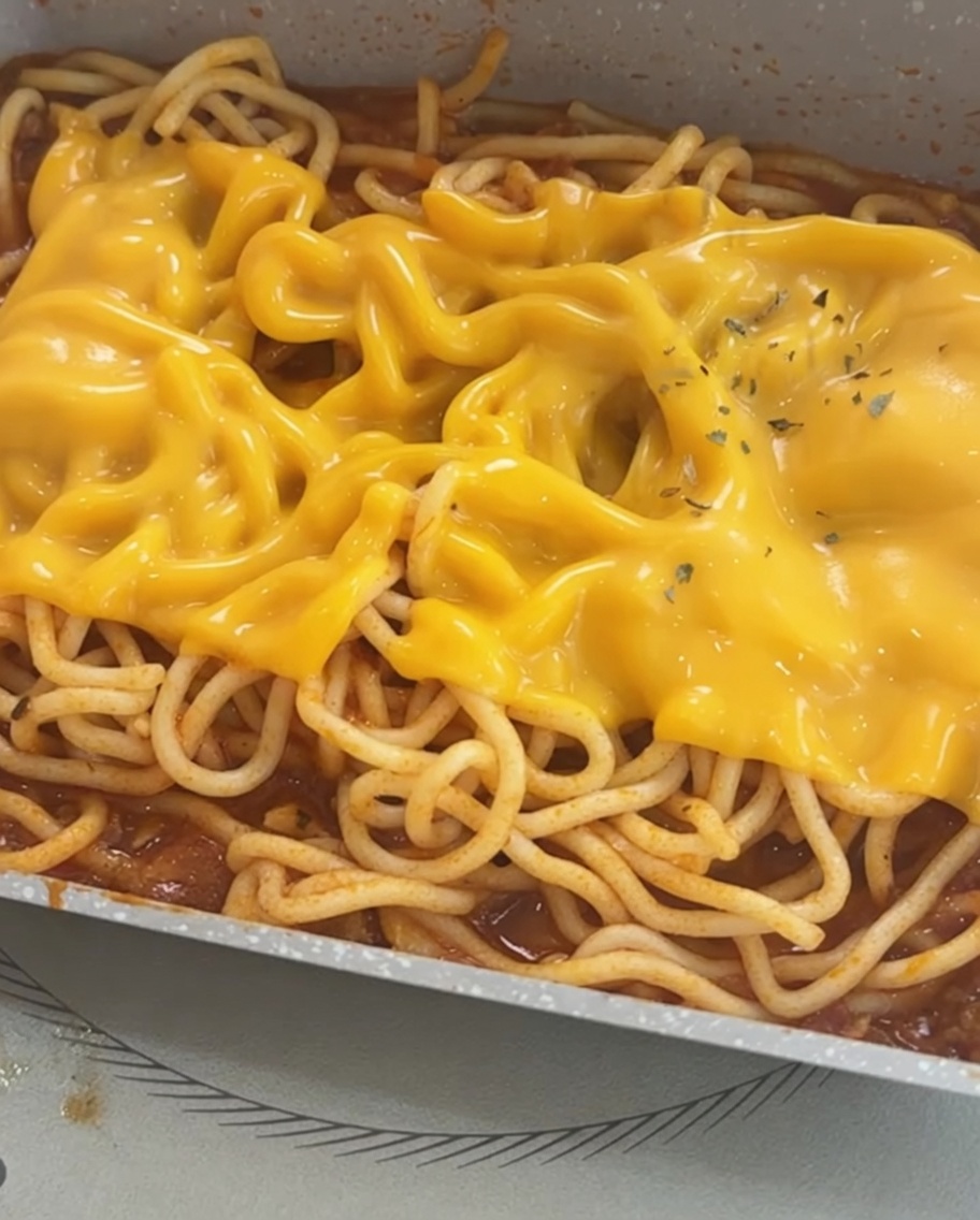 Spaghetti ricoperti di formaggio fuso, rifiniti con una guarnizione di scaglie di prezzemolo essiccato.