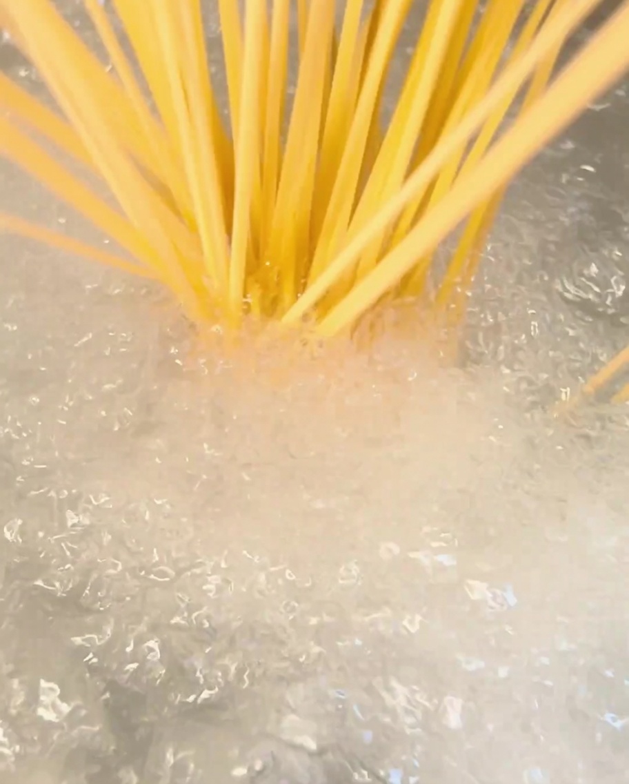 Un mazzetto di spaghetti secchi immerso in una pentola di acqua bollente.