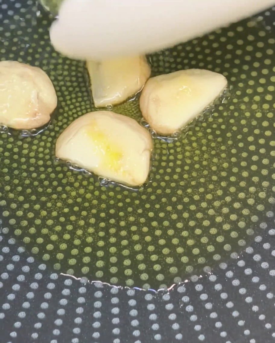 Spicchi daglio schiacciati che soffriggono nellolio doliva in una padella antiaderente.