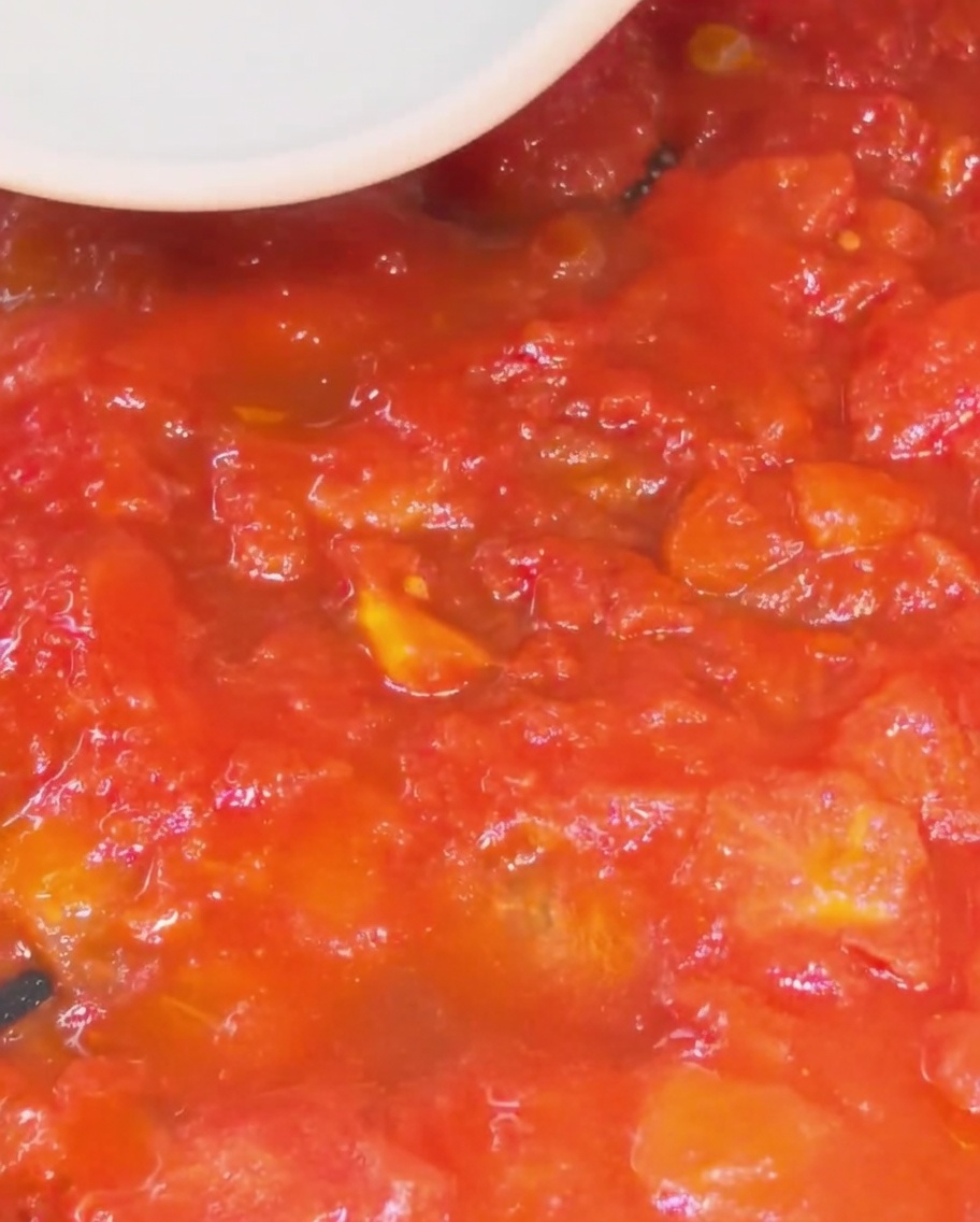 Primo piano di una spatola in silicone che schiaccia i pezzi di pomodoro in una salsa densa e liscia in padella.