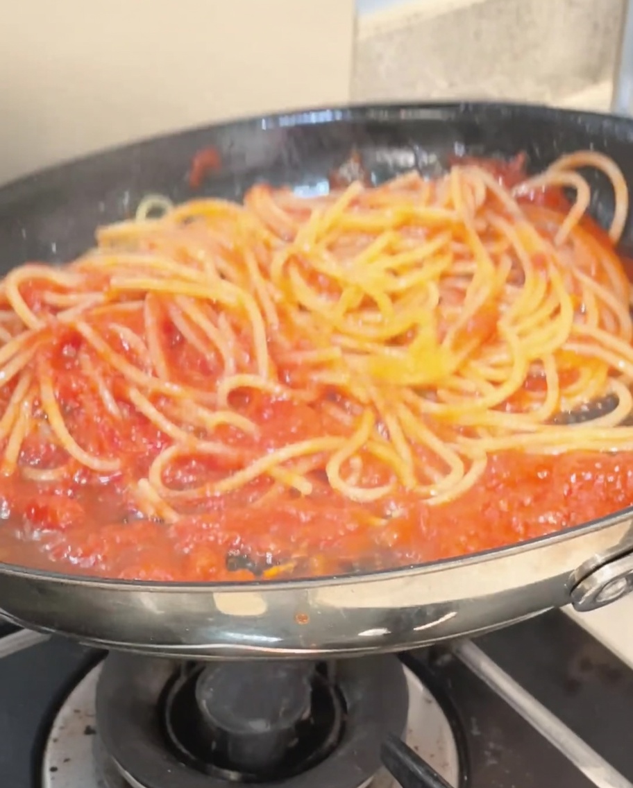 Spaghetti saltati con le pinze in una padella, perfettamente rivestiti di una vivace salsa al pomodoro rossa.