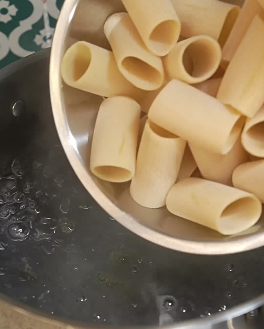Rigatoni crudi versati in una pentola di acqua in forte ebollizione.
