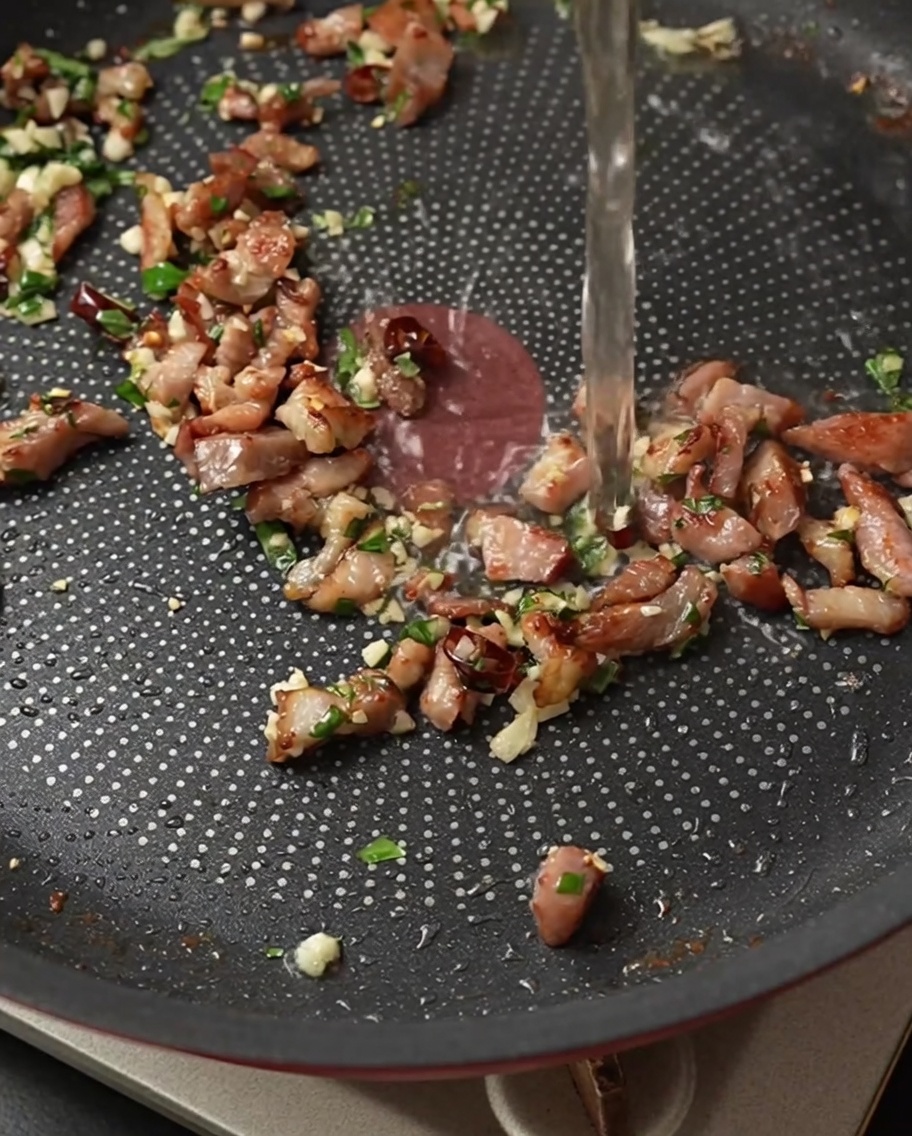 Vino bianco versato nella padella con pancetta, aglio, peperoncino e basilico.