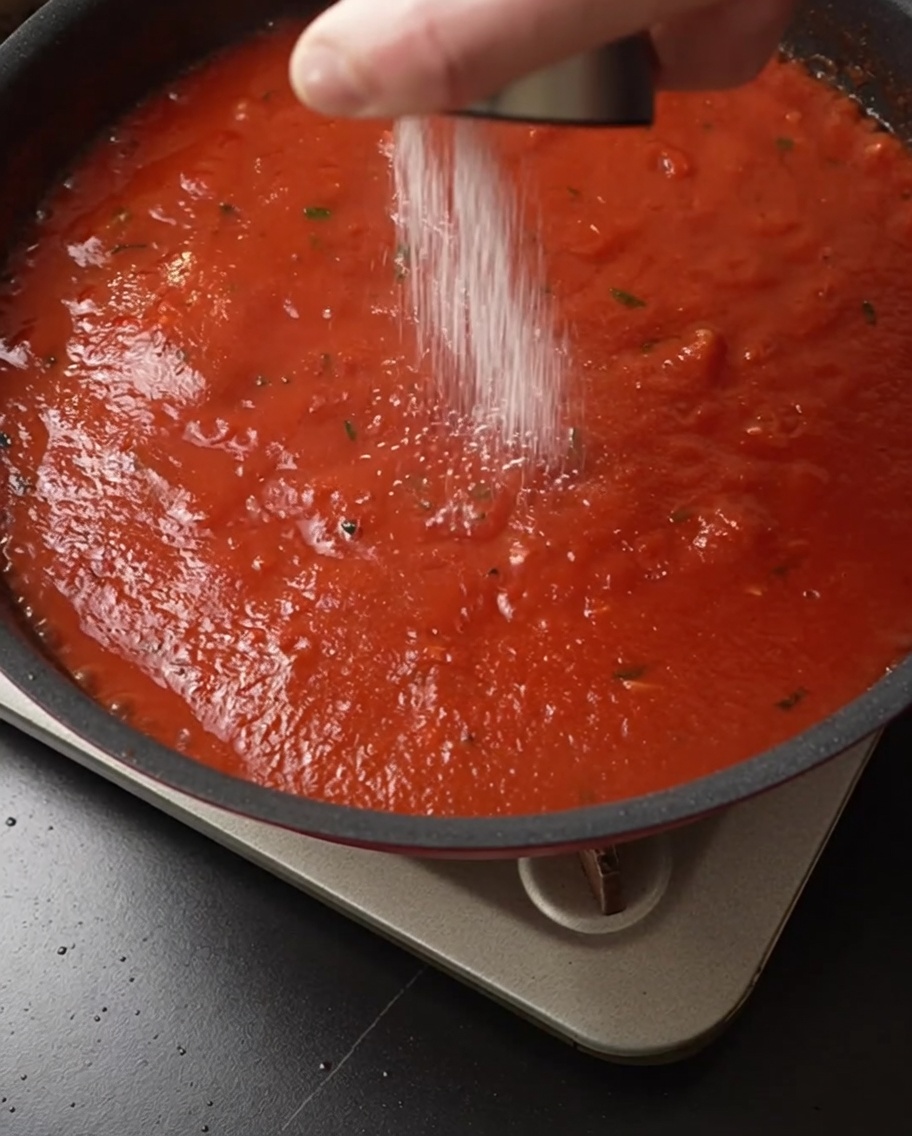 Sale spolverato sul sugo di pomodoro che sobbolle in padella.