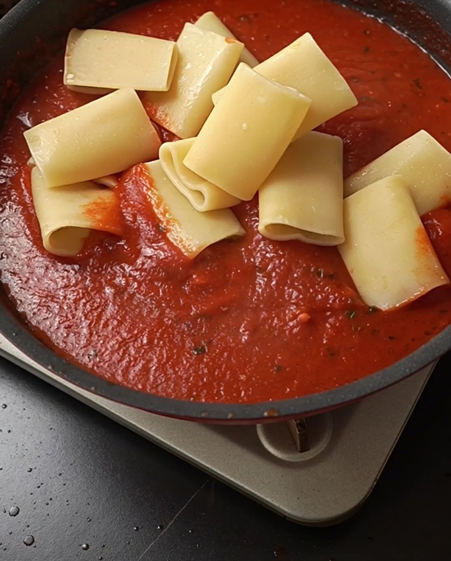 Rigatoni cotti uniti al vivace sugo di pomodoro in padella.