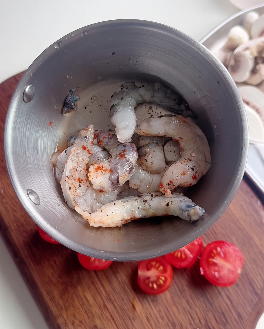 Primo piano di gamberi crudi in una ciotola di metallo conditi con pepe nero, peperoncino in polvere e una sottile miscela di amido.