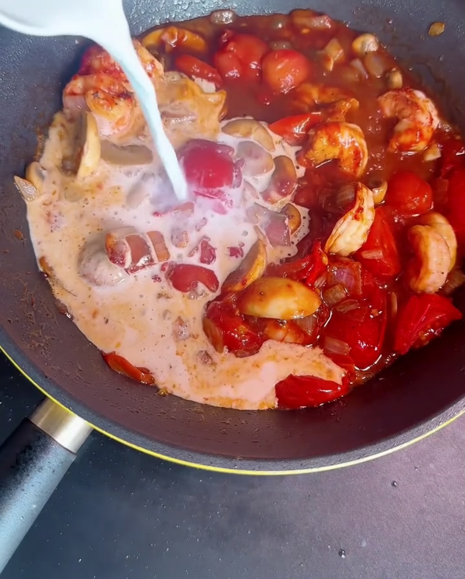 Latte e miscela di amido versati in una padella con gamberi, verdure e ingredienti per addensare il sugo.