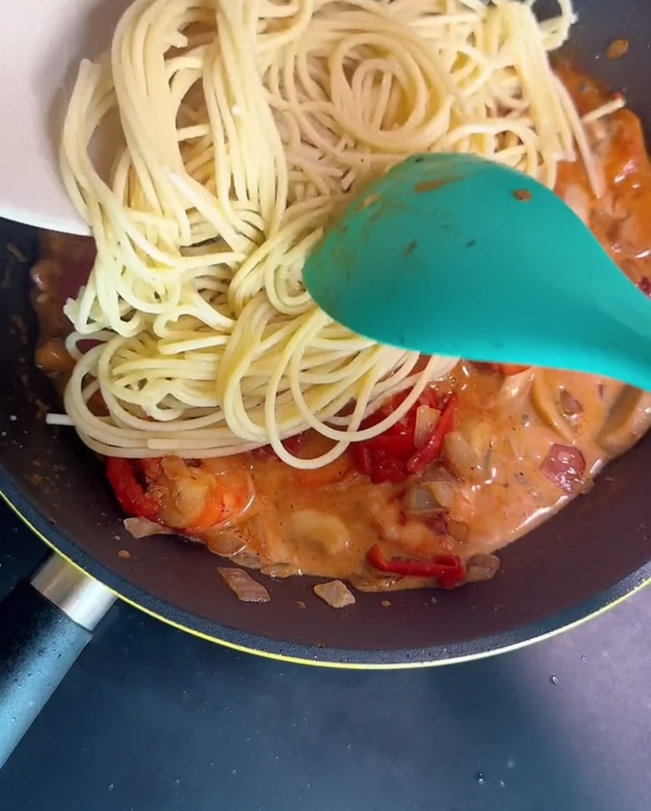 Spaghetti saltati in padella con una cremosa salsa di gamberi e funghi usando una spatola verde.