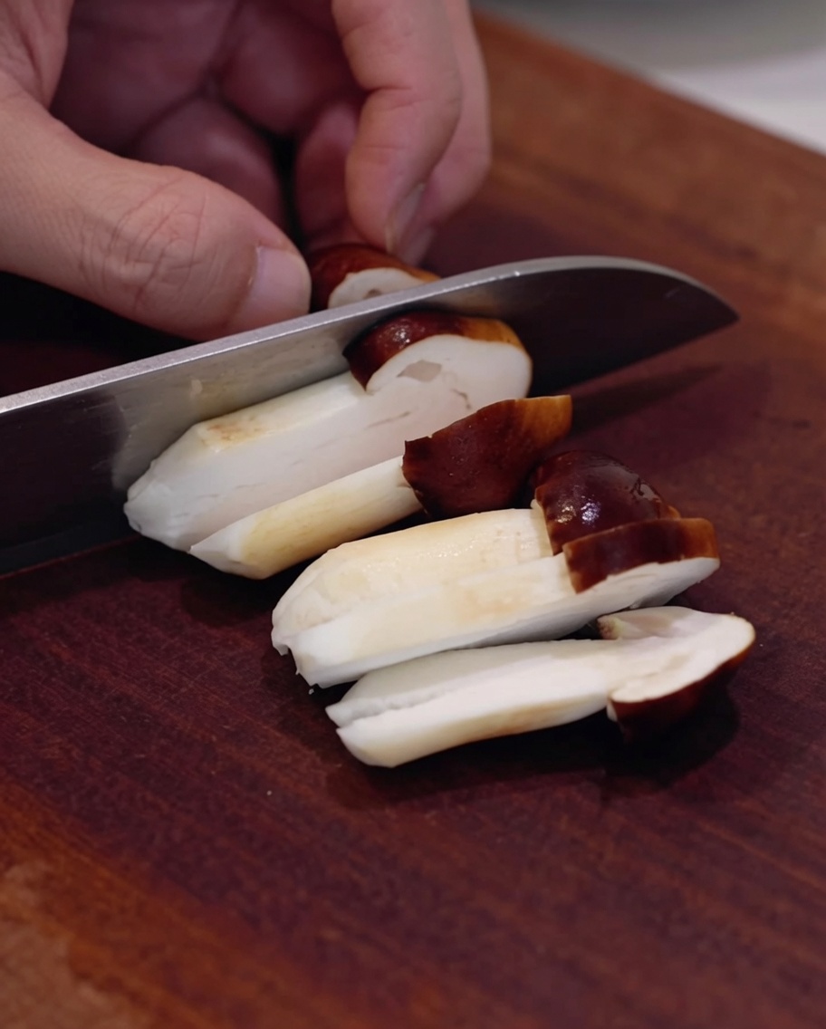 Funghi shiitake freschi affettati su un tagliere di legno.