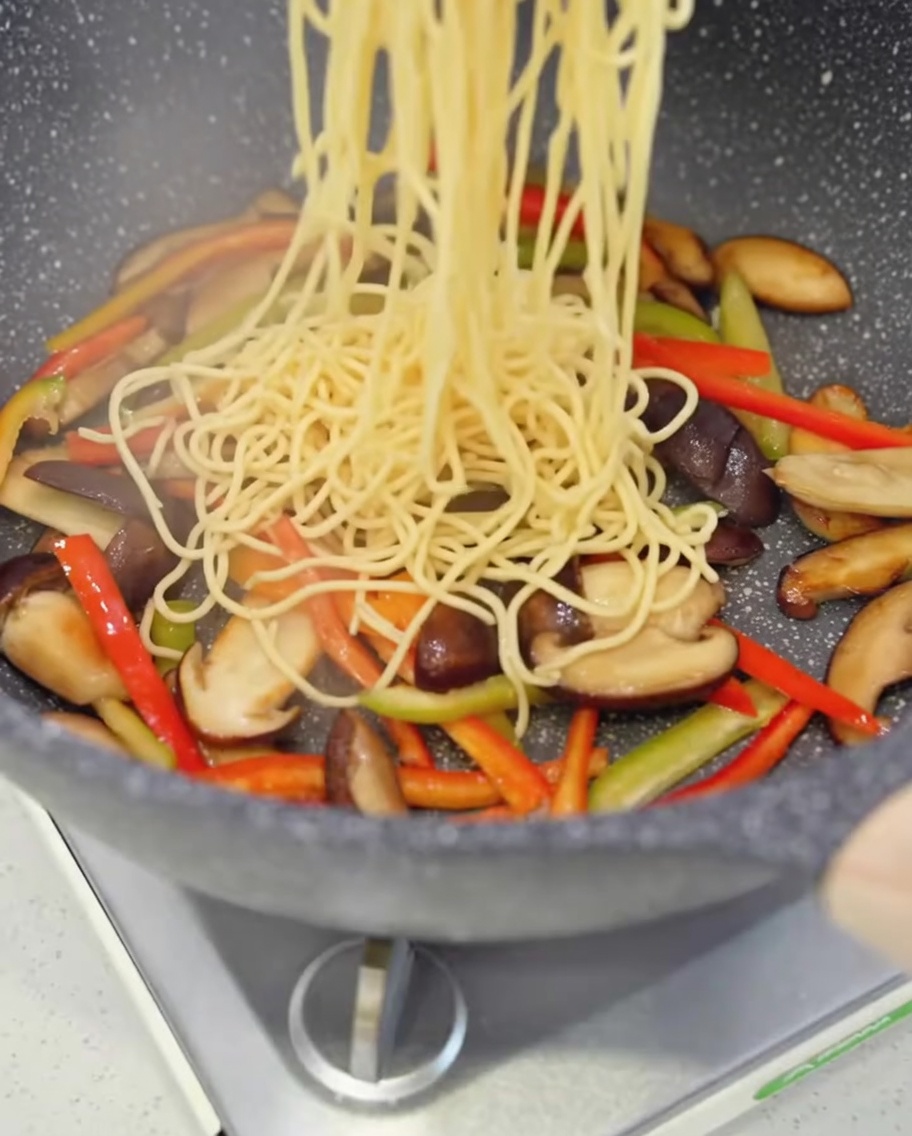 Spaghetti cotti aggiunti alla padella con funghi e peperoni.