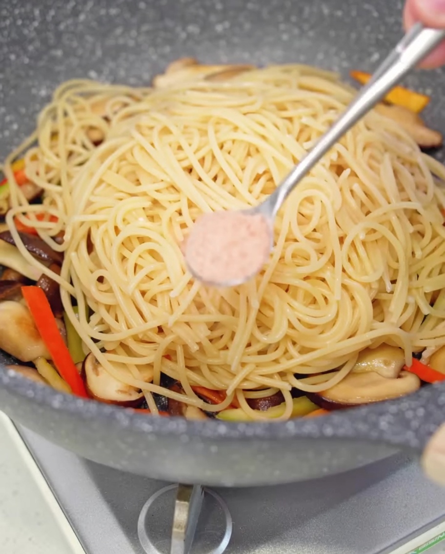 Un cucchiaino di sale aggiunto agli spaghetti in padella.