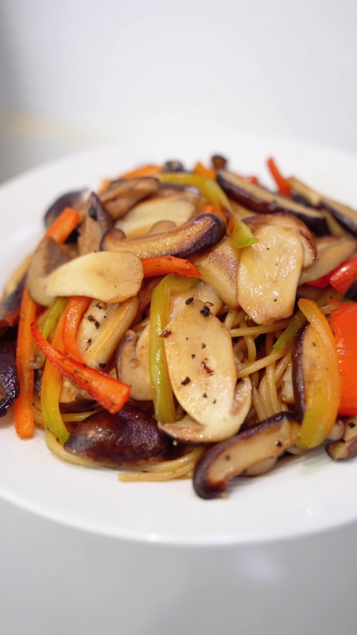 Spaghetti ai funghi al pepe nero serviti con shiitake e pioppini saltati, peperoni colorati e una spolverata di pepe fresco.