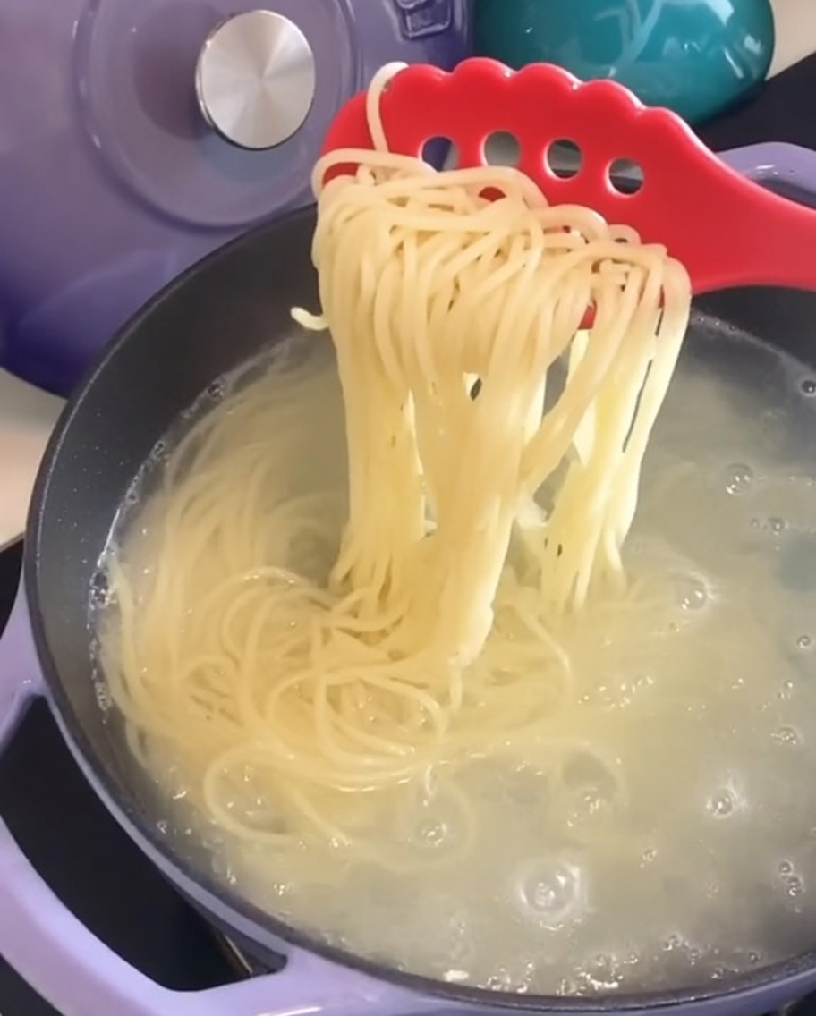 Spaghetti cotti sollevati dalla pentola con una pinza per pasta.
