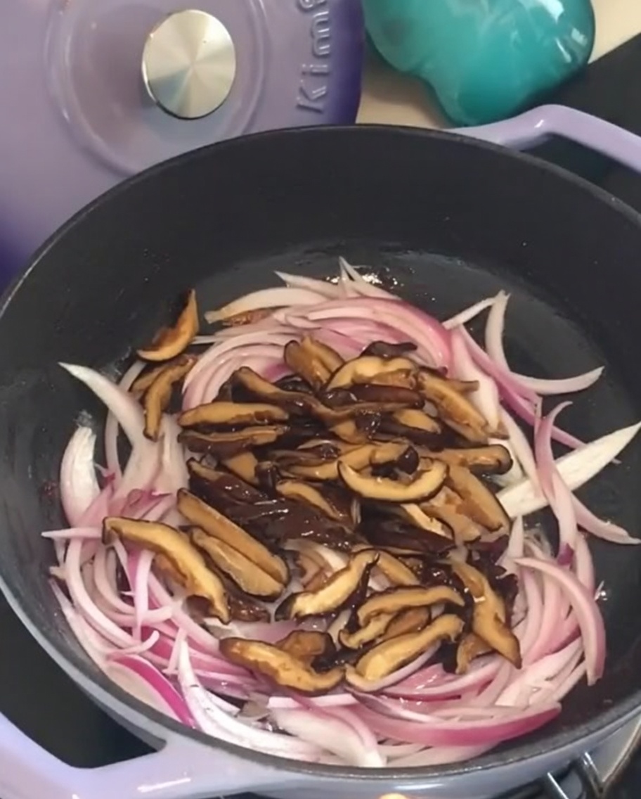 Funghi shiitake affettati aggiunti alla padella con la cipolla.