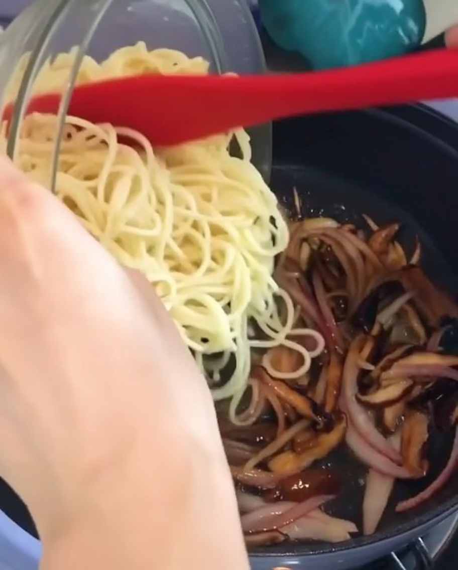 Spaghetti aggiunti in padella con funghi e cipolle.
