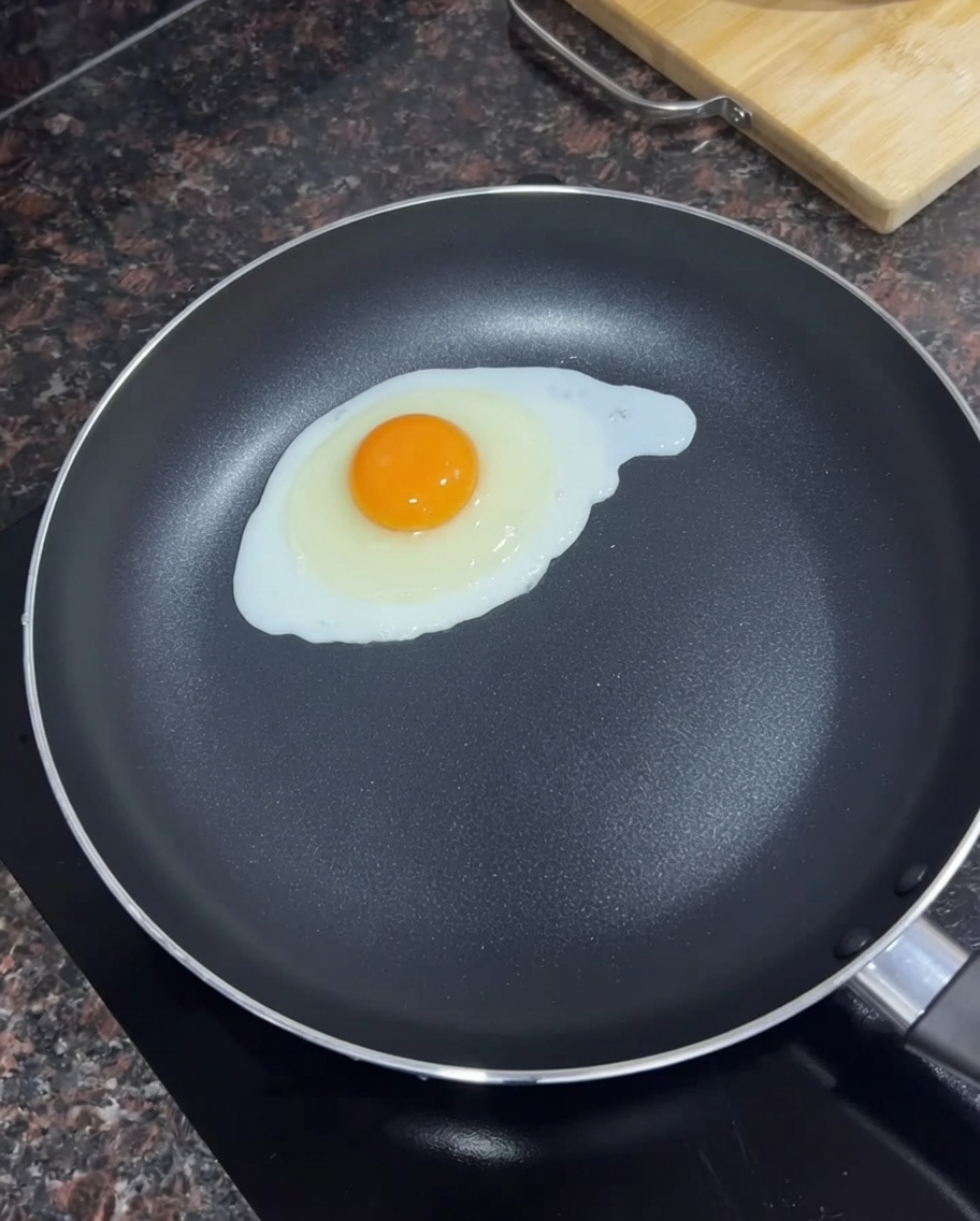 Un singolo uovo che frigge in una padella nera con burro fuso.