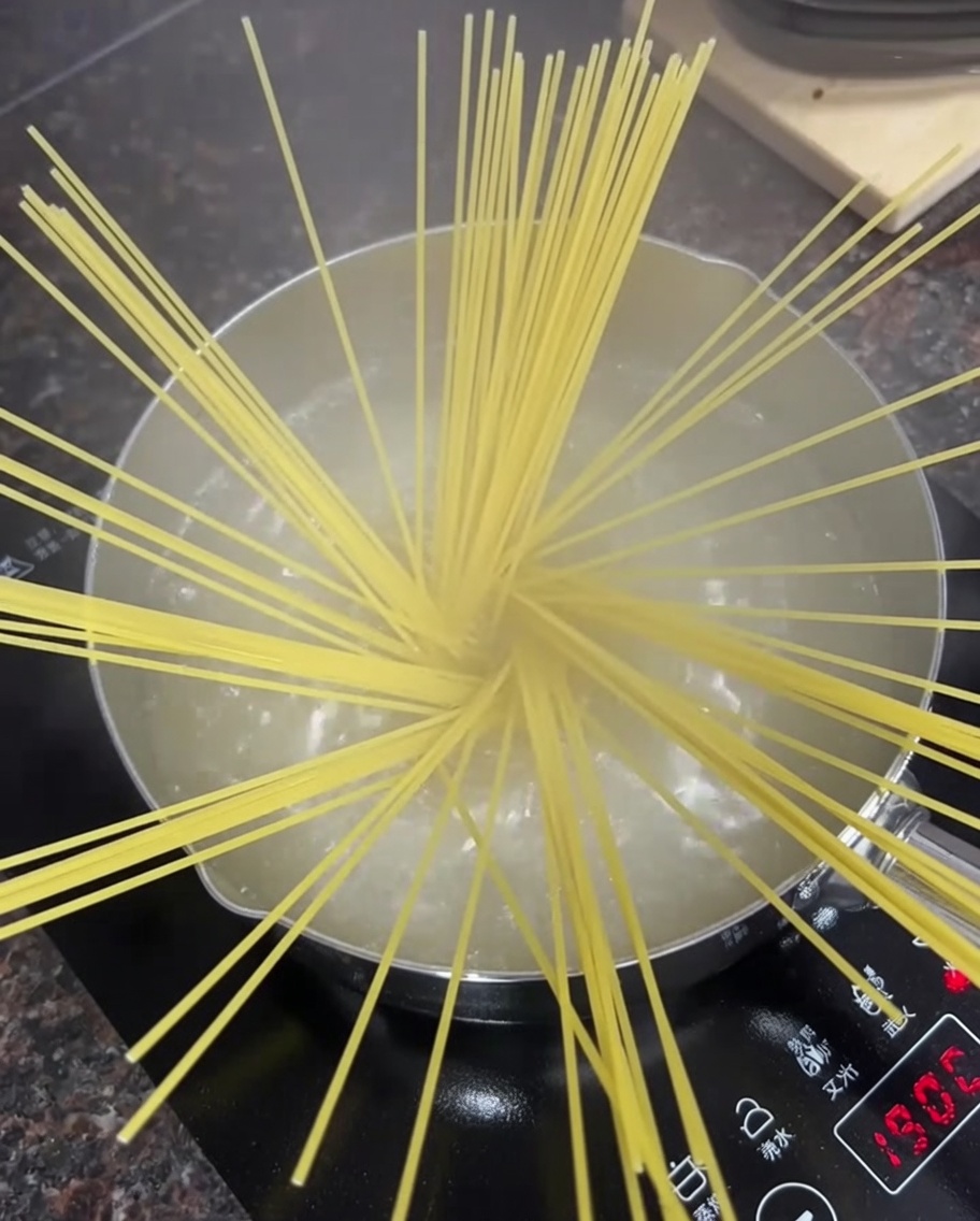 Spaghetti secchi in una pentola di acqua bollente sul fornello.
