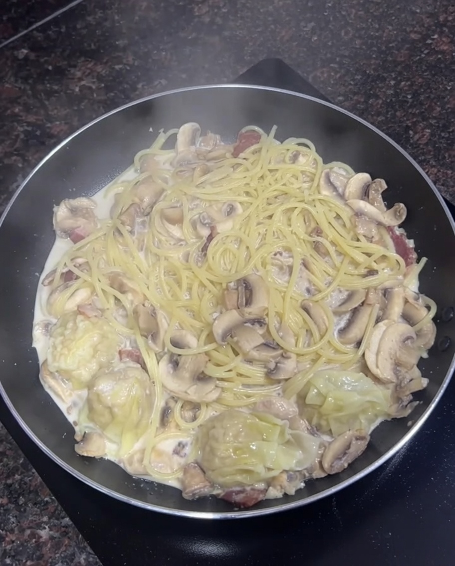 Padella riempita con spaghetti cremosi, funghi e alcuni wonton cotti.