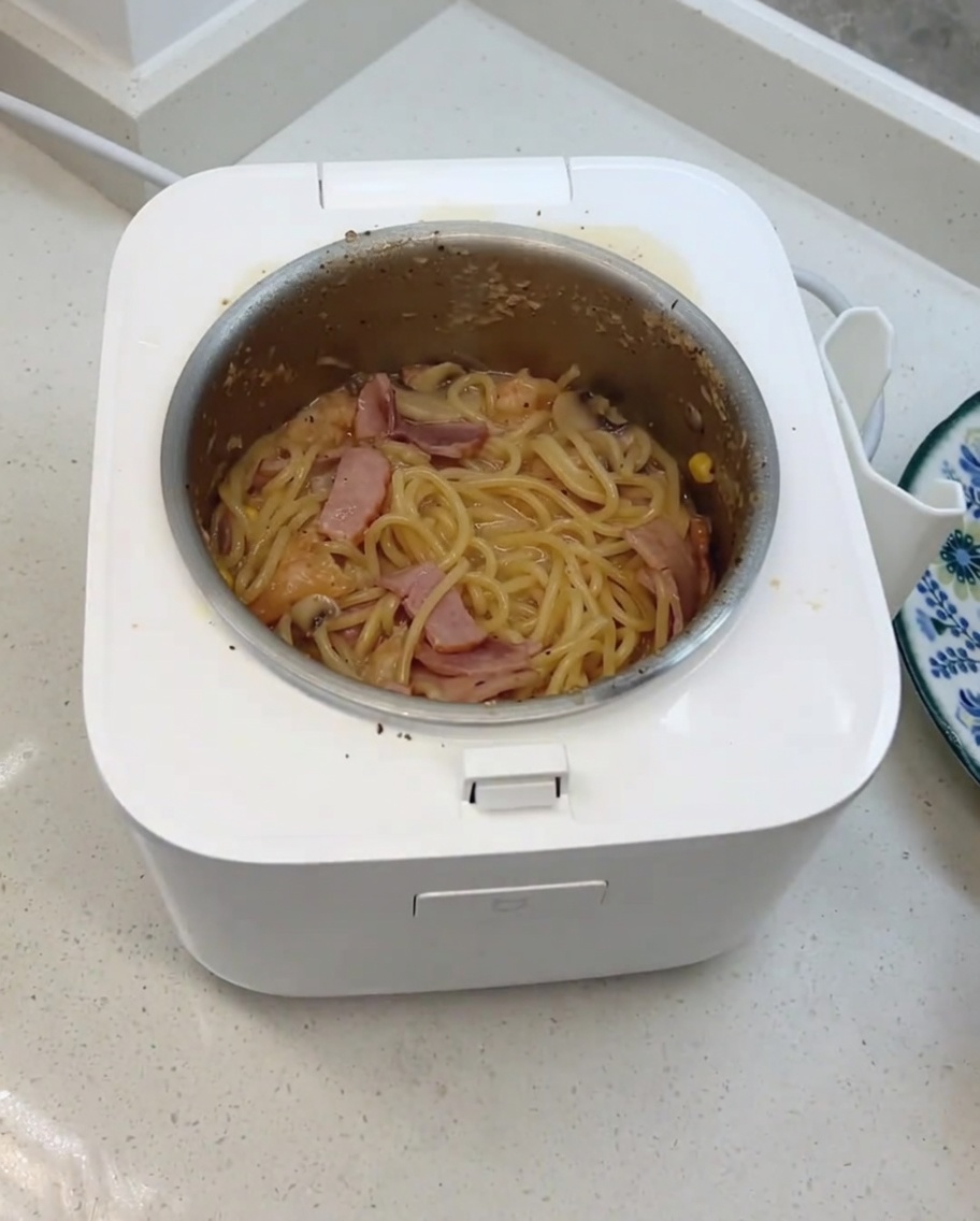 Gli spaghetti cremosi ai funghi finiti mentre vengono mescolati con formaggio e cubetti di formaggio aggiunti nella cuociriso.