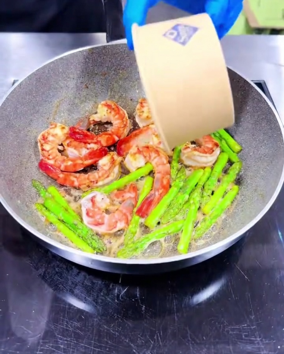 Aglio tritato mescolato nella padella con gamberi e asparagi in cottura.
