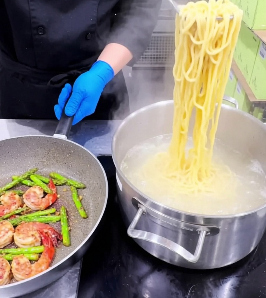 La pasta viene aggiunta in una padella contenente gamberi cotti, asparagi e aglio.