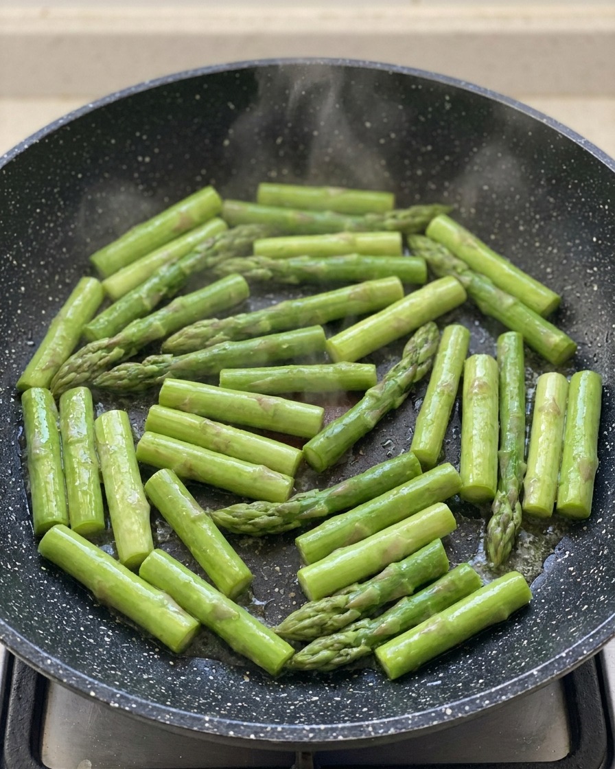 Asparagi verdi tagliati che sfrigolano in una padella scura.