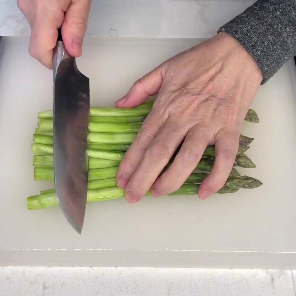 Gambi di asparagi pelati tagliati a segmenti uniformi su un tagliere bianco.