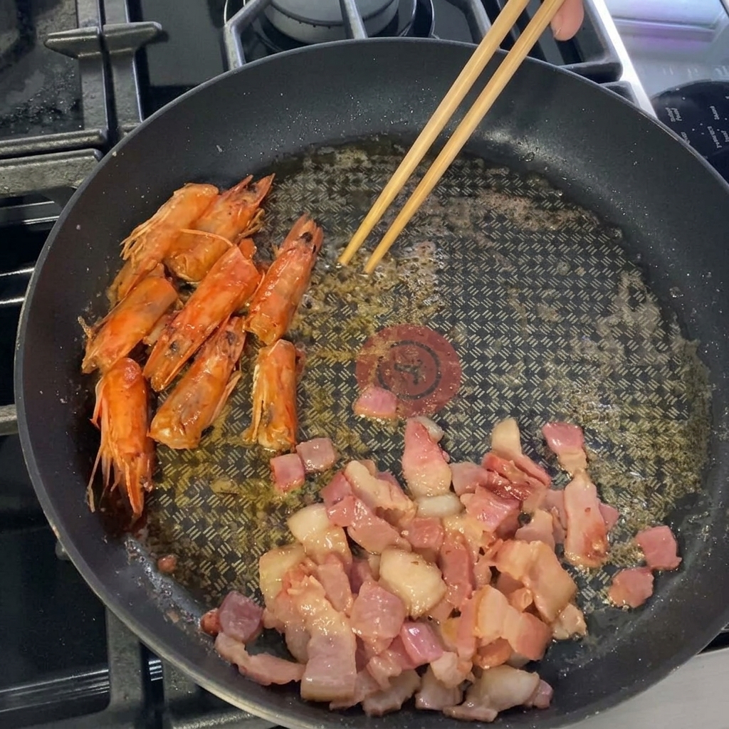 Gamberi grandi puliti messi nella padella accanto alla pancetta e alle teste di gamberi.