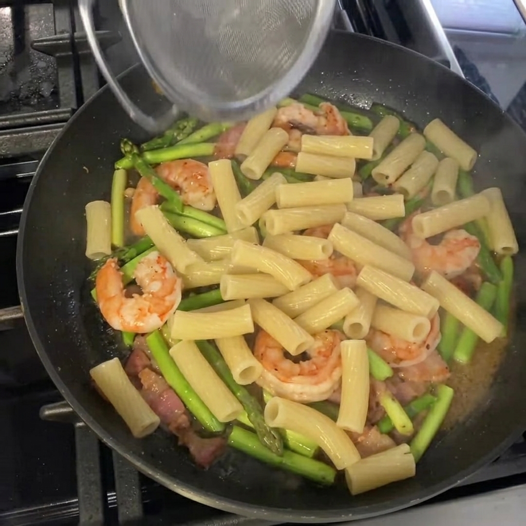 Rigatoni cotti saltati nella padella con gli asparagi e i gamberi, pronti per il condimento finale e la guarnizione.